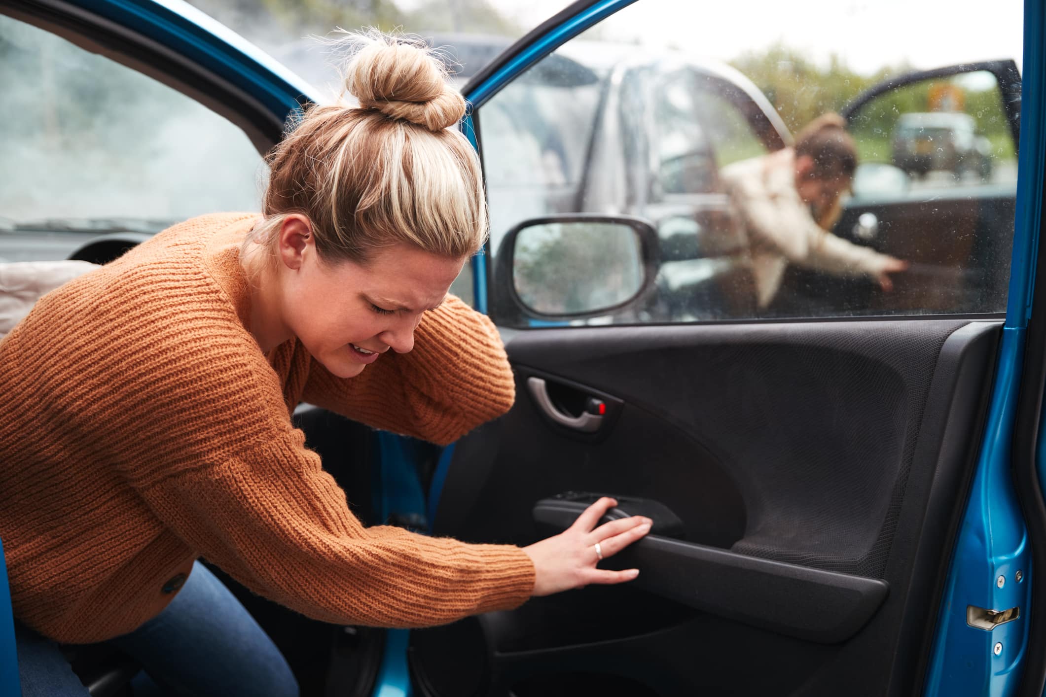A woman holding her neck in pain as she gets out of her car after a car accident.