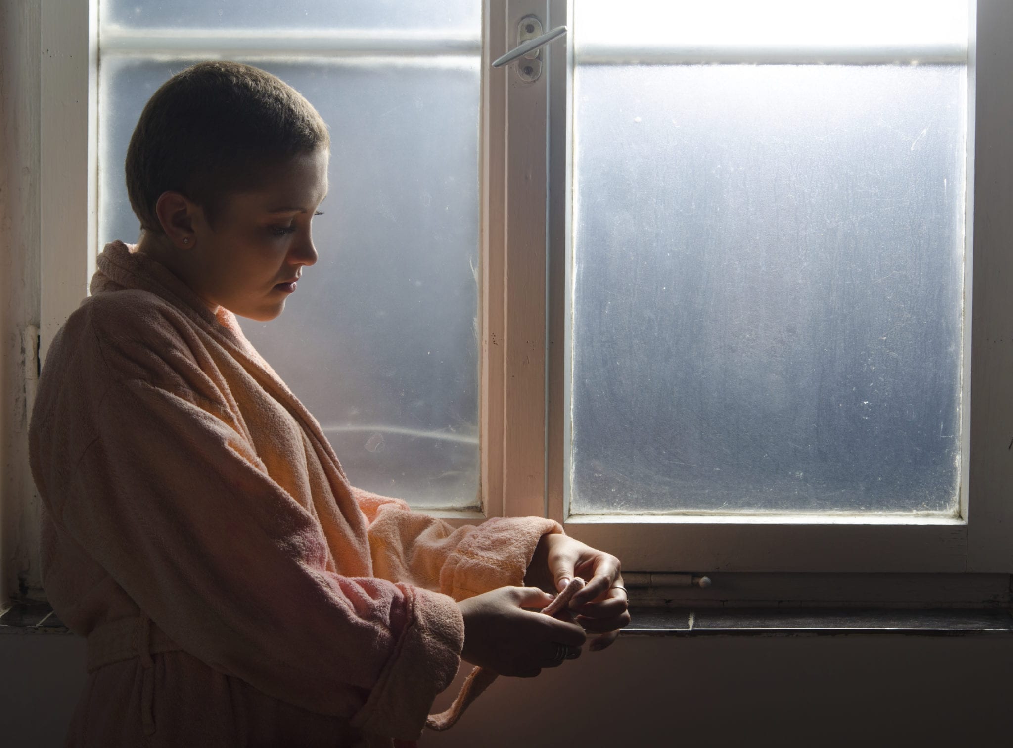 Young Cancer Patient Staring Out A Window Inside A Hospital
