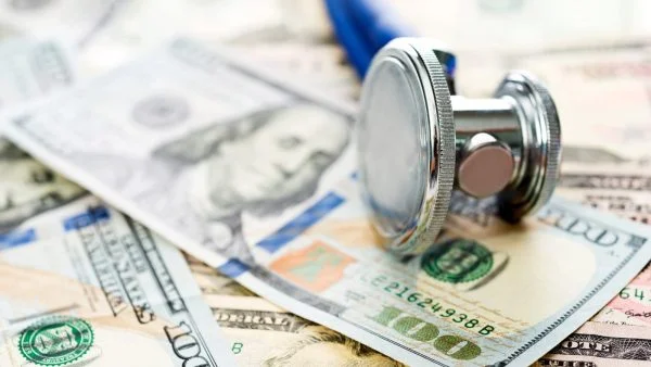 A stethoscope lying on a stack of $100 and $50 bills.