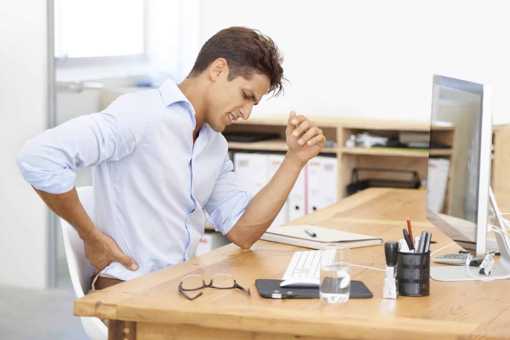 Young Man Experiencing Lower Back Pain At Desk Stock Photo