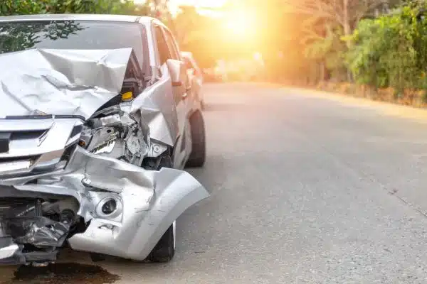 A silver car with a badly damaged front end is on the side of the road after an accident.