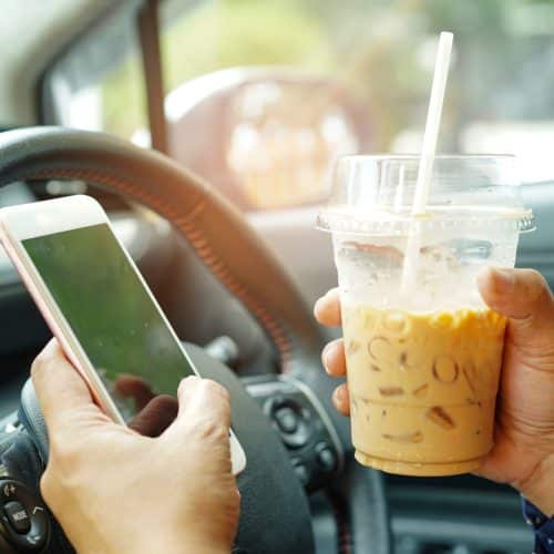 A driver holds their cell phone and a coffee instead of the wheel.