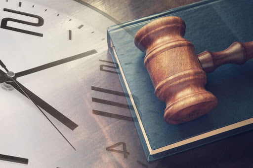 A book with a gavel resting on it is overlaid with the image of a clock.