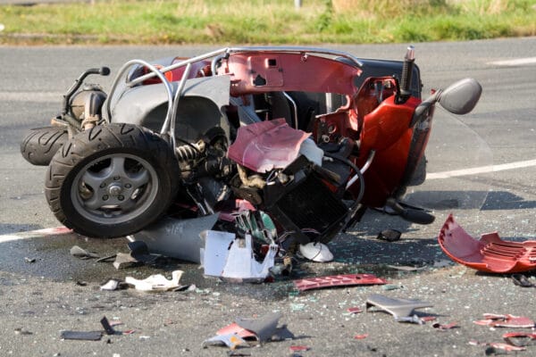 A damaged, red motorcycle sits in pieces on the side of the road after an accident.