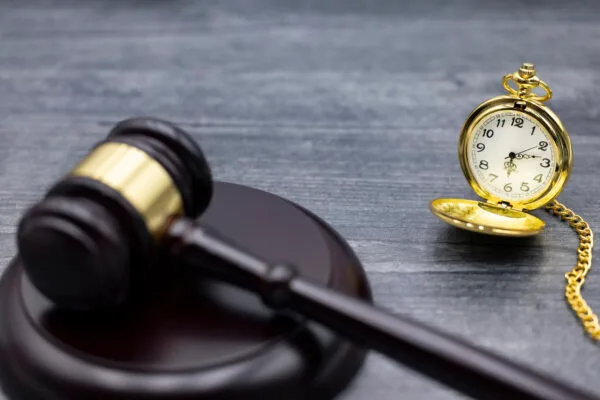 A gavel and block next to a pocket watch on a gray table.