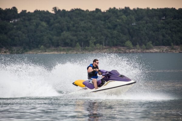 A man on a jet ski in the middle of a lake, with trees in the background.