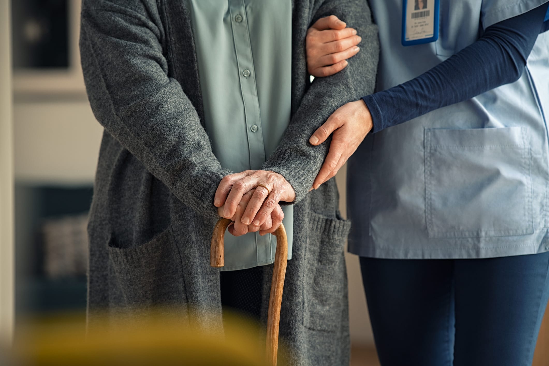 An elderly person using a cane is assisted by a nursing home caretaker.
