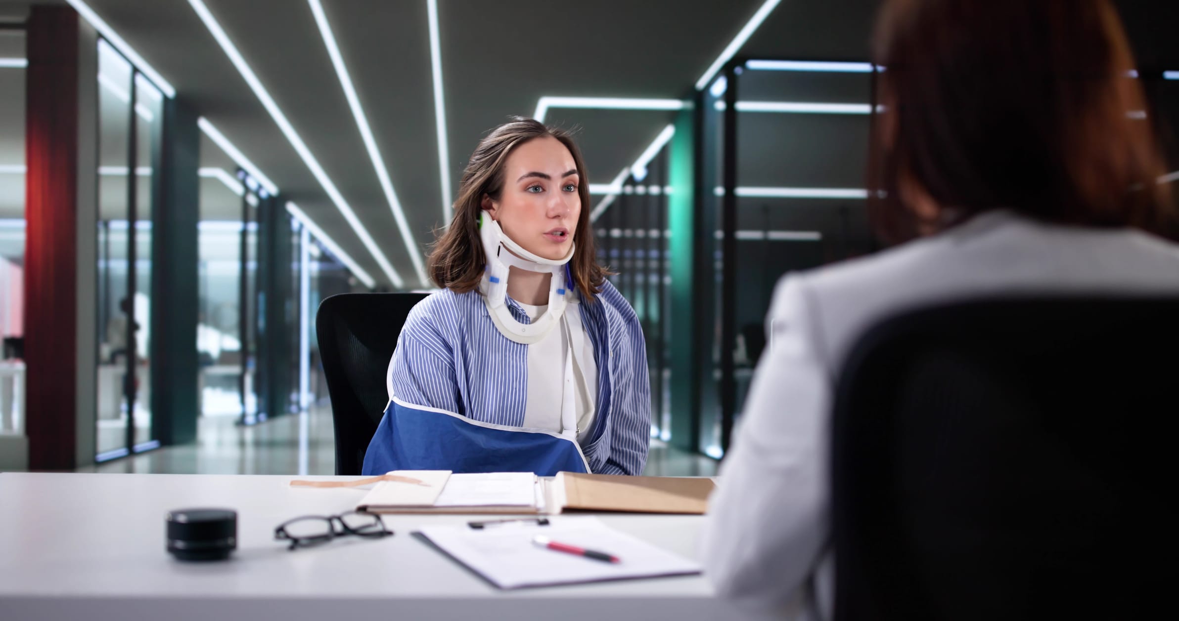 An injured woman with a neck brace and arm in a sling speaks to a personal injury lawyer.