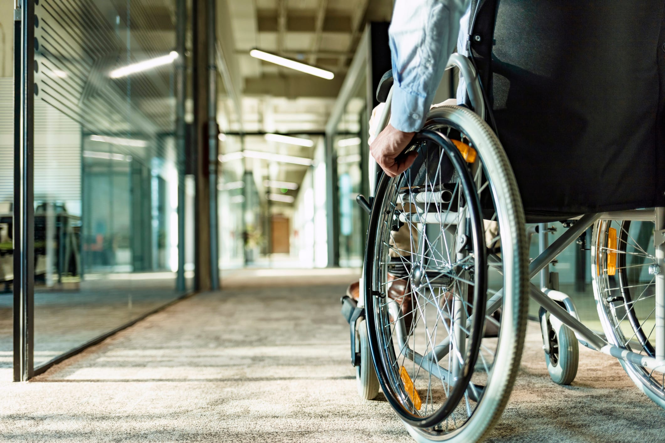 A person in a wheelchair going down a carpeted hallway in an office building.