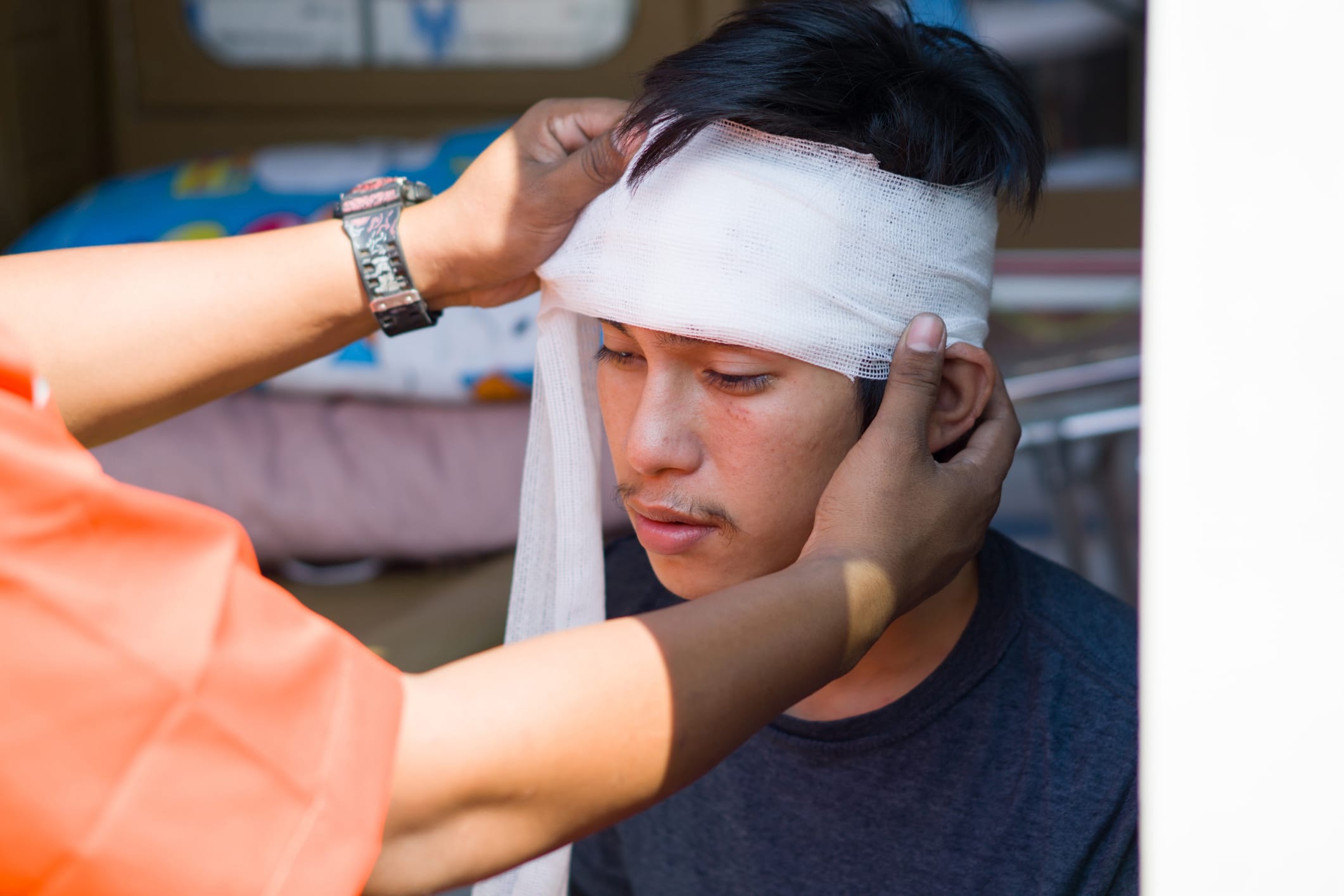 A man has his head bandaged by a medical professional after an accident.