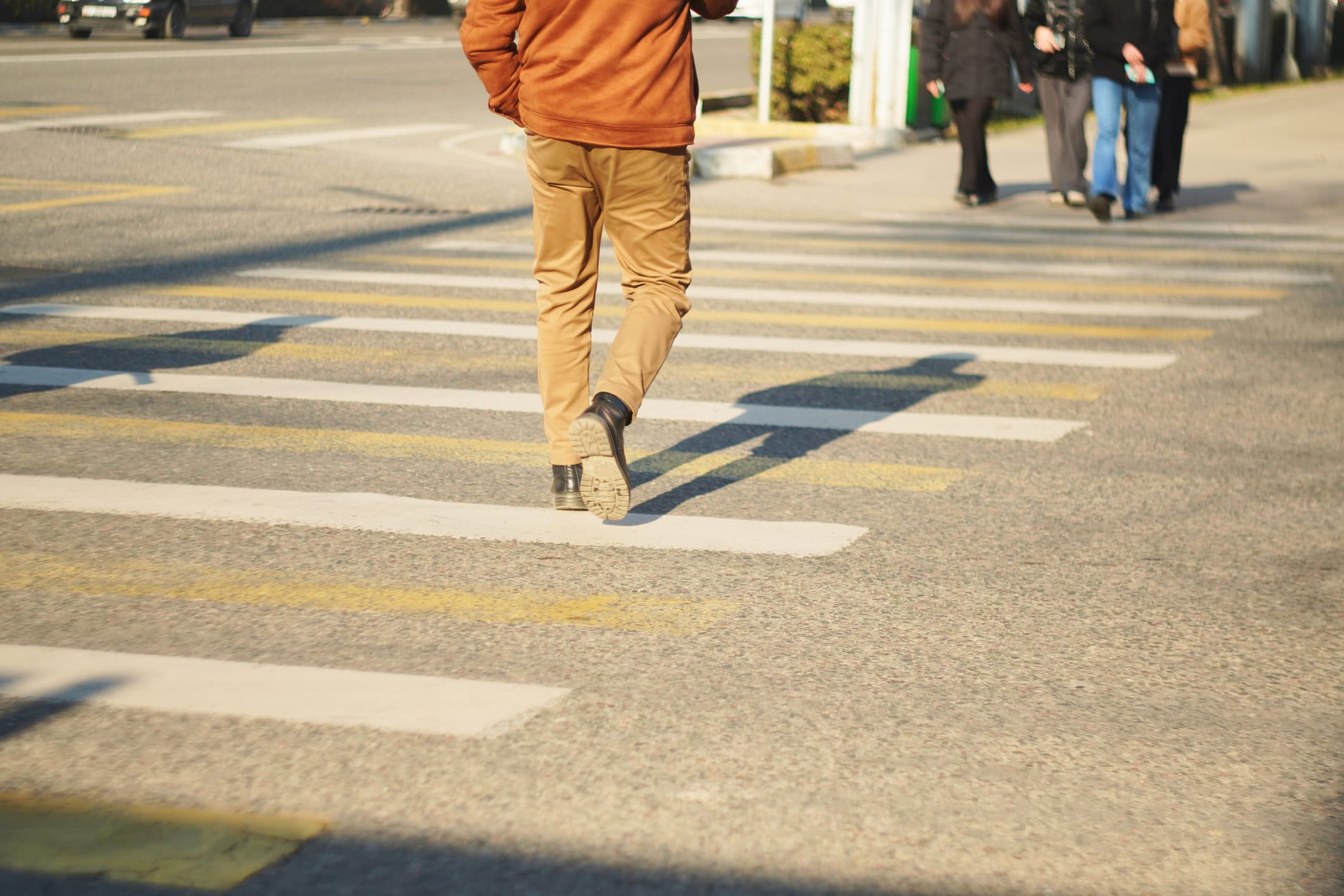 A person crossing a street at a crosswalk. A separate group of people is crossing in the opposite direction.