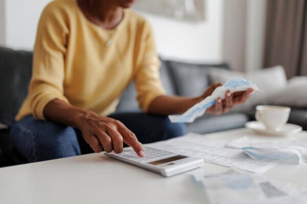 A woman sits on her couch, using a calculator while looking at paperwork.