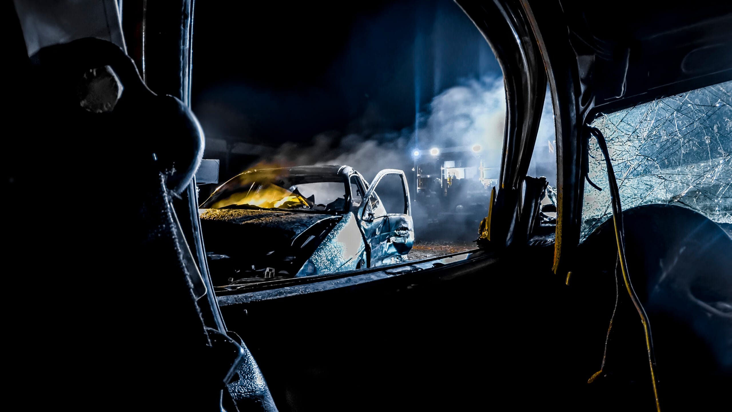 View from inside a wrecked car. You can see a damaged windshield, and the other damaged and smoking car nearby.
