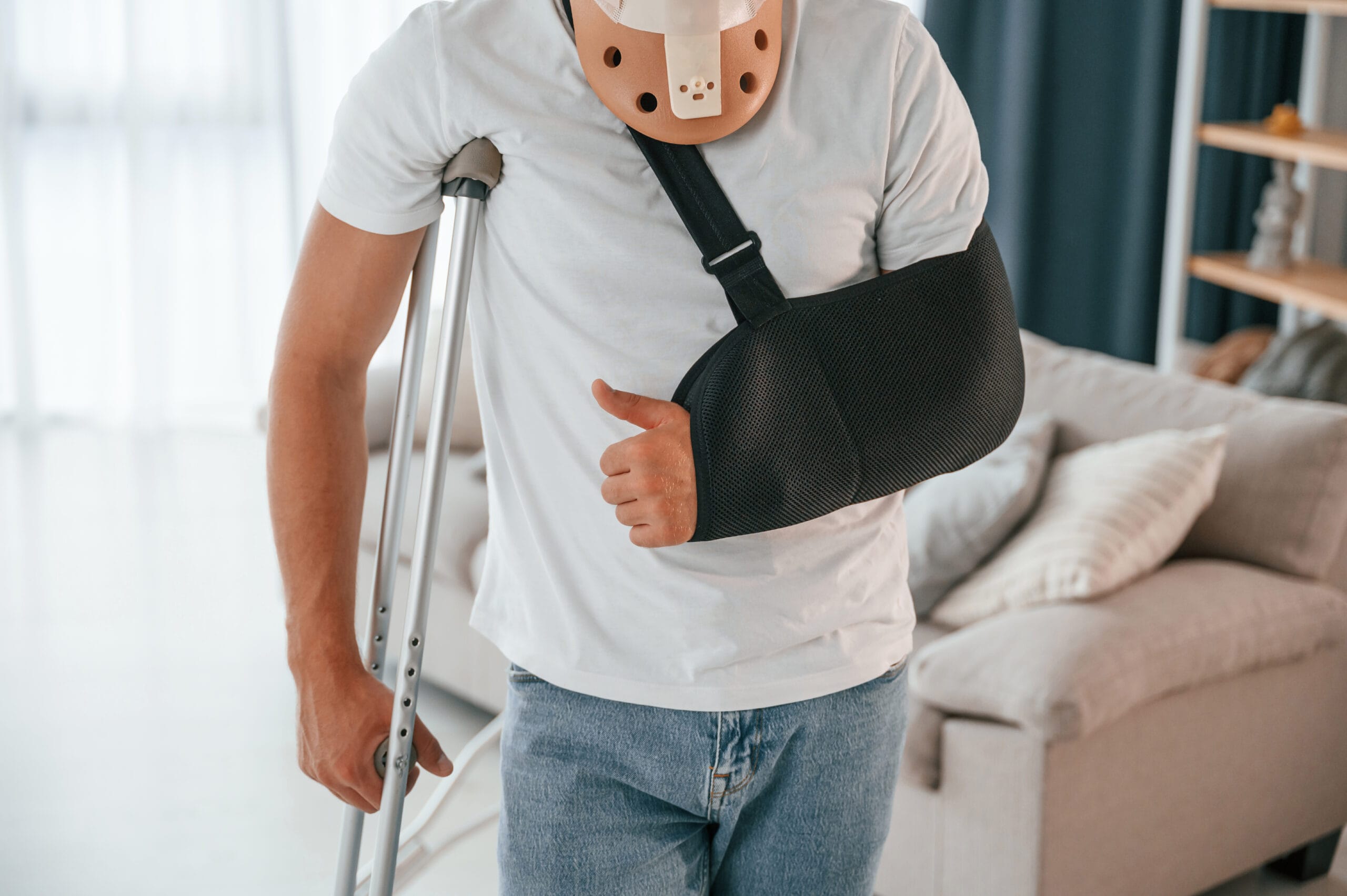 Close-up of an injured man wearing a neck brace and arm sling using crutches.