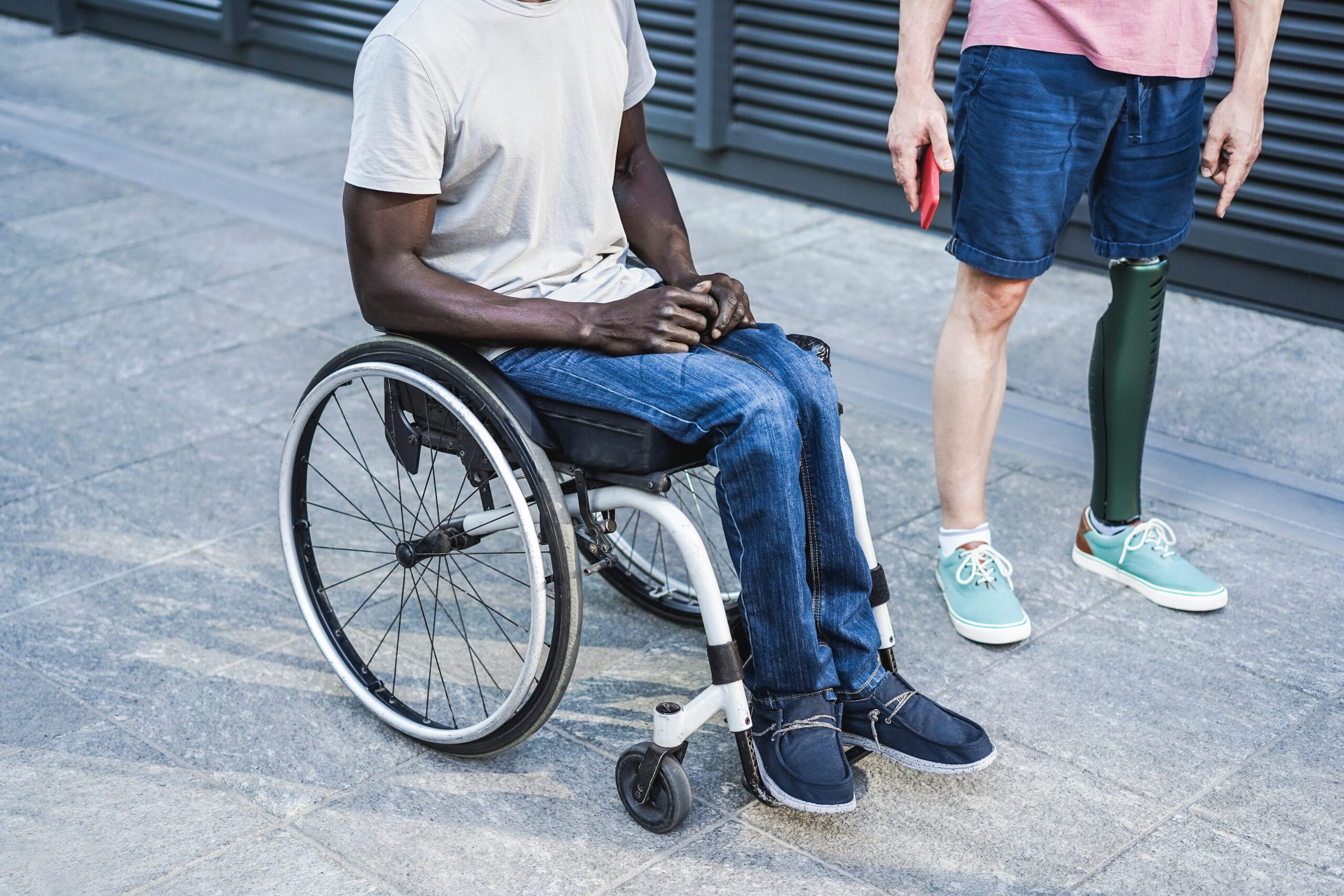 Two individuals, one in a wheelchair and one standing with a prosthetic leg.