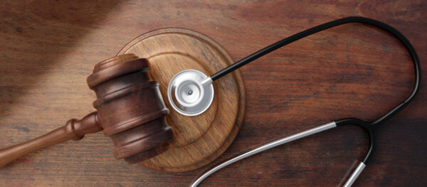 A stethoscope, gavel and block sit on a wooden desk.