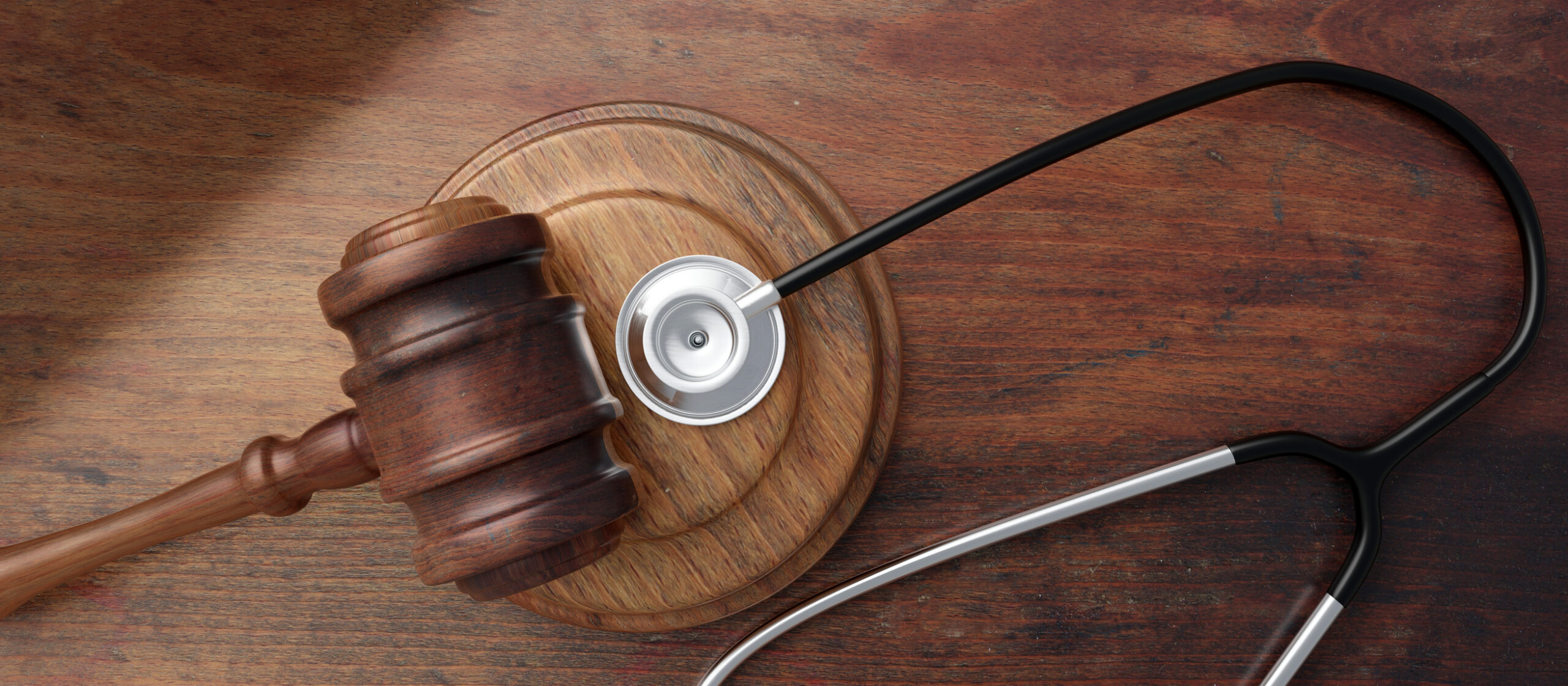 A stethoscope, gavel and block sit on a wooden desk.